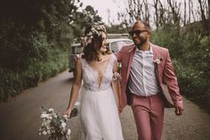 a bride and groom walking down the road holding flowers in their hair as they hold hands