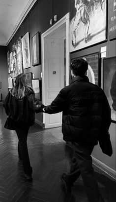 a man and woman are walking through an art gallery holding hands while looking at pictures on the wall