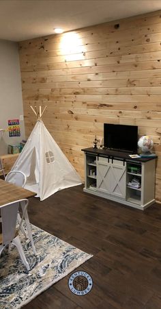 a living room with wood paneling and a white teepee tent on the floor