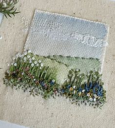 a close up of a piece of cloth with flowers and grass on the ground next to it