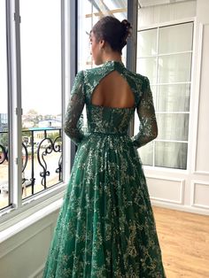 a woman standing in front of a window wearing a green dress with long sleeves and an open back