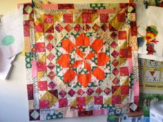 an orange and green quilt hanging on a wall next to other items in a room