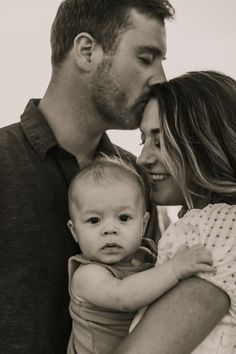 a black and white photo of a man holding a baby in his arms while the woman holds him