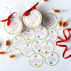 six christmas gift tags with red ribbon on white table top next to candy candies