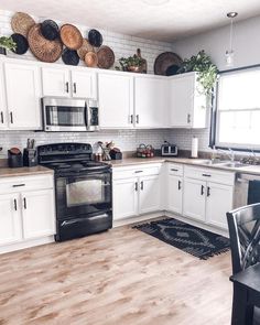 a kitchen with white cabinets and wood floors, black appliances and wicker baskets on the wall