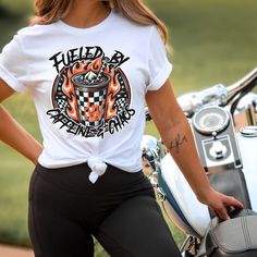 Fuel your rebellious spirit with our Fueled by Caffeine and Chaos shirt! This electrifying design features a black and white checked iced coffee cup adorned with a rocker skeleton hand, surrounded by flames, lightning bolts, and a bold checkered pattern. It's the perfect blend of edgy 80s and 90s vibes, making it a must-have for all coffee lovers with an edge. Whether you're a super cool soccer mom or just someone who thrives on caffeine-fueled adventures, this shirt is sure to add a jolt of exc Rebellious Cotton Tops With Graphic Print, Rebellious Cotton Top With Graphic Print, Rebellious Cotton Graphic Print Tops, Rebellious Crew Neck T-shirt For Summer, Rebellious Summer Crew Neck T-shirt, Rebellious Crew Neck T-shirt For Streetwear, Rebellious Streetwear T-shirt With Crew Neck, Rebellious Cotton T-shirt With Graphic Print, Caffeine And Chaos Shirt