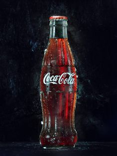 an empty coca cola bottle sitting on top of a black surface with water droplets all over it