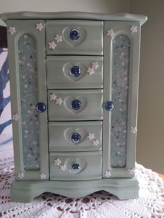 a small green cabinet with stars painted on the doors and drawer fronts, sitting on a doily