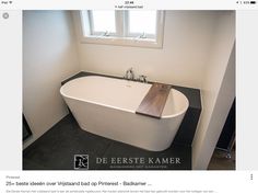 a white bath tub sitting under a window next to a wooden sink faucet