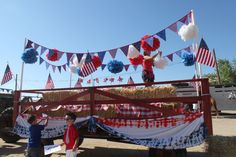 two children are standing on the back of a truck decorated with american flags and pom poms