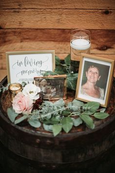 a wooden barrel with flowers and pictures on it, next to a candle that reads the loving memory