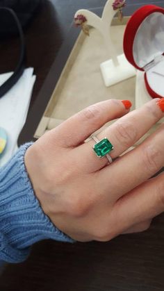 a woman's hand with an emerald ring on it and a box in the background