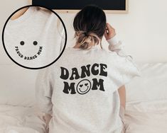 a woman sitting on top of a bed wearing a sweatshirt with the words dance mom printed on it