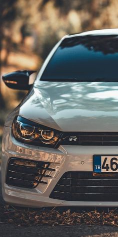 the front end of a silver car parked on top of a street next to trees