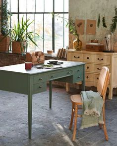 a green table with two chairs and a potted plant on it in front of a window