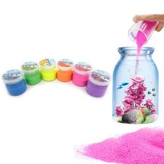 a jar filled with pink sand next to other colored powders and a hand pouring it into the jar