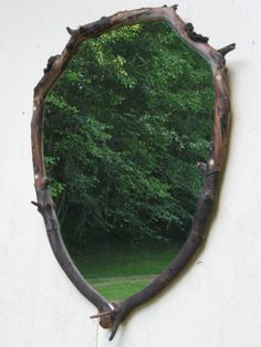 a mirror hanging on the side of a white wall with trees in the back ground