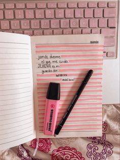 an open notebook with writing on it next to a computer keyboard and a pink pen