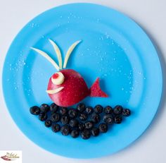 a blue plate topped with fruit and veggies shaped like a fish on top of berries