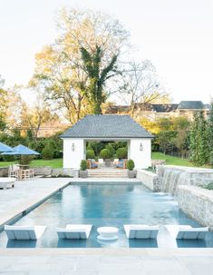 an outdoor pool with lounge chairs and umbrellas next to the swimming area in front of it