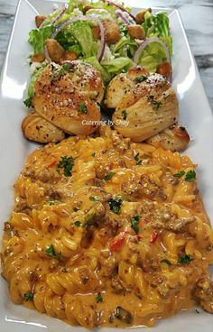 pasta with meat, bread and salad on a white plate in front of a marble table