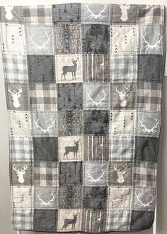 a quilt hanging on the wall with deers and trees in grey, white and black squares