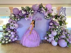 a woman in a purple dress is standing next to balloons and garlands on the wall