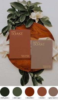 two brown books sitting on top of a wooden table next to green leaves and flowers