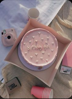 a pink birthday cake on a plate next to a camera and some other things around it