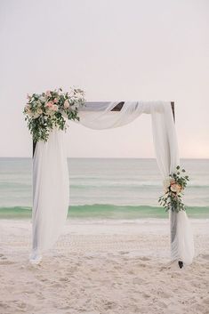 an outdoor wedding setup on the beach with white draping and pink flowers at sunset