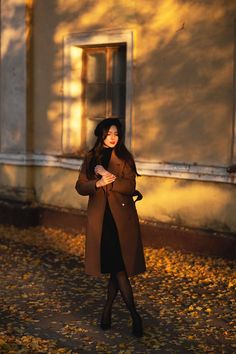 a woman standing in front of a building wearing a brown coat and black tights