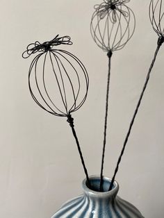 three wire flowers in a blue vase with white wall behind them and black string wrapped around the stems