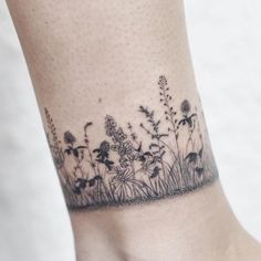 a tattoo on the ankle of a woman with flowers and grass growing out of it