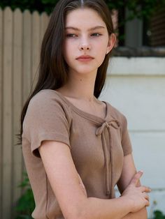 a young woman with her arms crossed standing in front of a fence