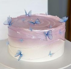 a pink and white cake with blue butterflies on the frosting is sitting on a plate