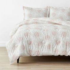 a white bed with pink flowers on it in a room next to a wooden floor