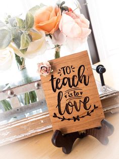 a wooden sign that says to teach is to love with flowers in the back ground