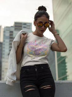 a woman in ripped jeans and a t - shirt is leaning against a wall with her hand on her head