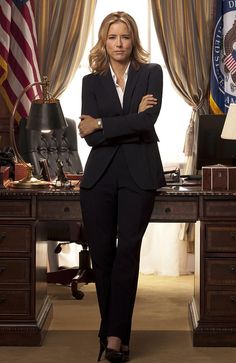 a woman standing in front of a desk with an american flag behind her