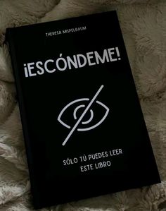 a black book sitting on top of a bed next to a white blanket with the words escondeme written in spanish