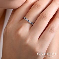 a woman's hand with a diamond and sapphire ring on her left hand, wearing a white gold band