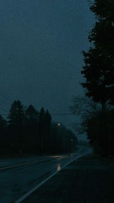 an empty street at night with the lights on and trees in the foreground,