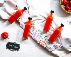 three bottles of hot sauce sitting on top of a table next to a bowl of tomatoes