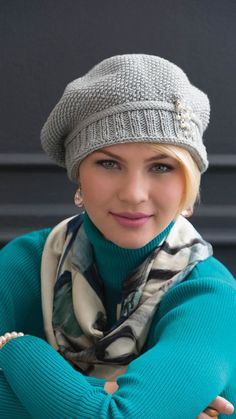 a woman wearing a hat and scarf posing for the camera with her arms folded over her chest