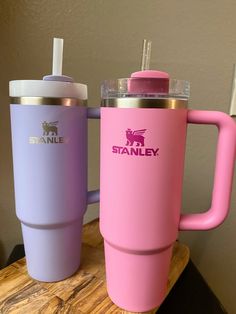 two pink and purple travel mugs sitting on a wooden table next to each other