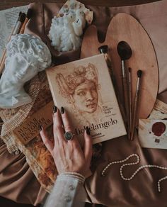 a woman's hand on top of a book surrounded by art supplies and other items