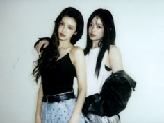 two young women standing next to each other in front of a white wall and one is holding a black purse