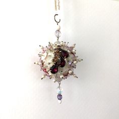 a necklace with beads and crystals hanging from a hook on a white surface, in the shape of a sunburst