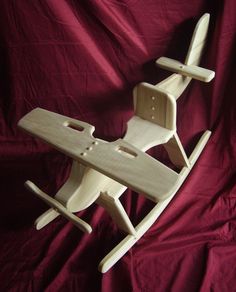 a wooden toy airplane sitting on top of a red cloth covered bed sheet with it's seat up