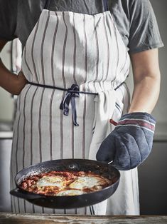 a person in an apron holding a skillet with food on it